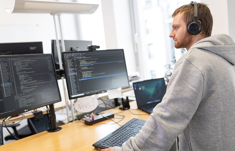 WhereGroup Softwareentwickler mit Kopfhörern bei konzentrierter GIS-Programmierung - praxisnahe Geo-IT-Entwicklung mit modernem Arbeitsplatz-Setup