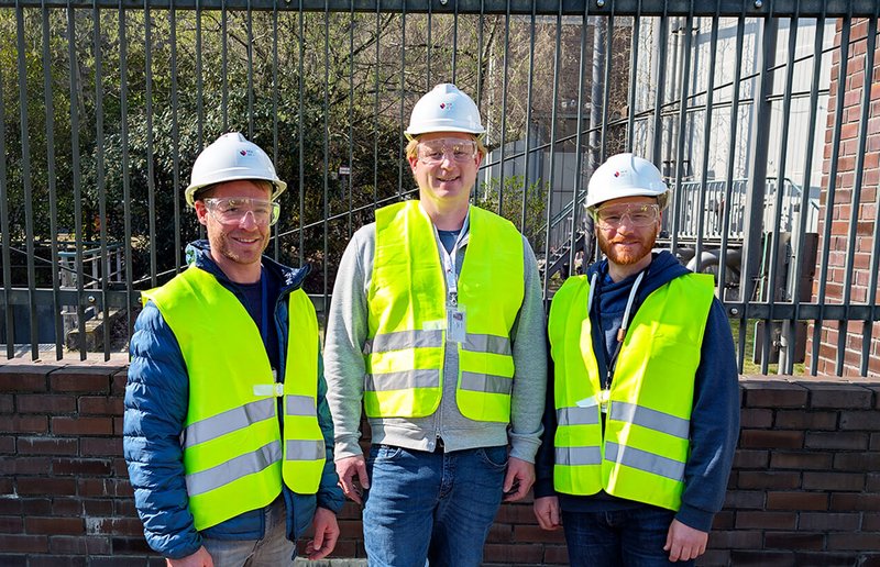 Drei WhereGroup-GIS-Experten mit gelben Sicherheitswesten und weißen Helmen an einem Kunden-Standort